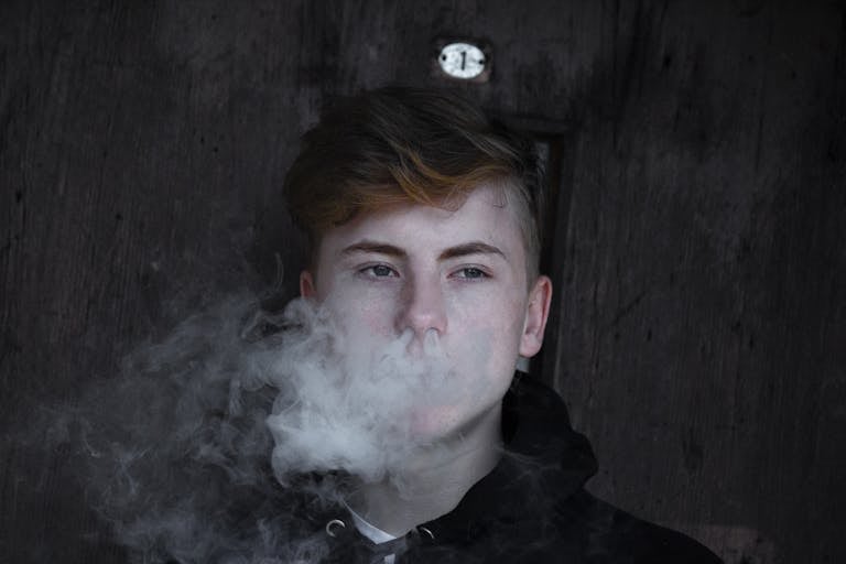 Close-up portrait of a young man exhaling smoke, creating a moody effect.