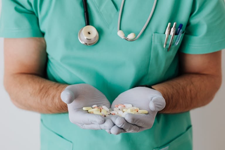 A healthcare professional in uniform holding a variety of pills in gloved hands.