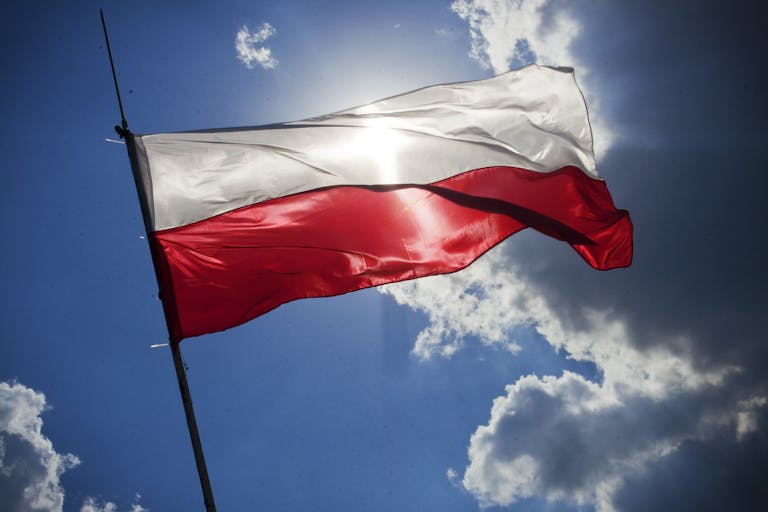 A Polish flag flutters against a bright blue sky with clouds, symbolizing national pride.