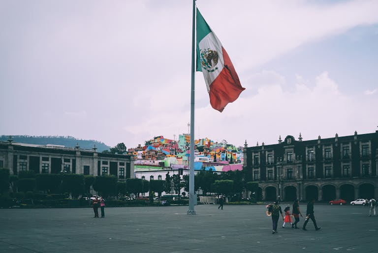 Colorful cityscape of Toluca with large Mexican flag in the foreground, vibrant buildings in the backdrop.