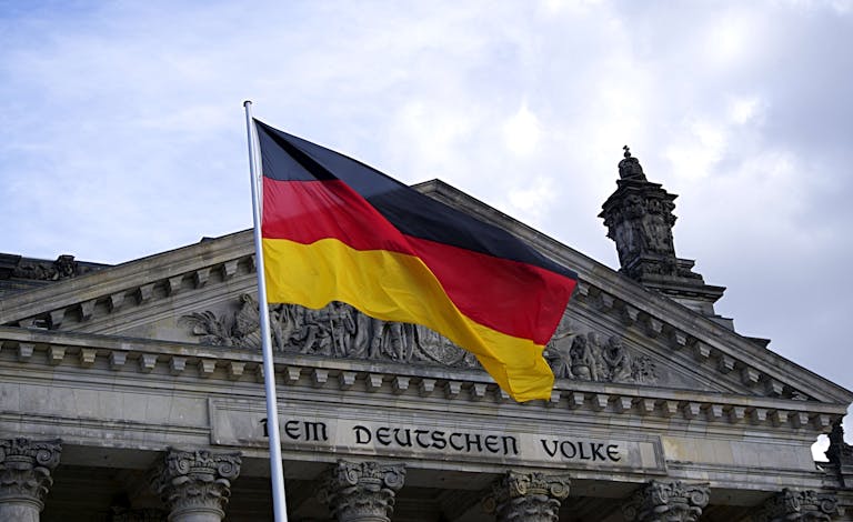 German national flag waving in front of the Reichstag building in Berlin, a symbol of democracy.