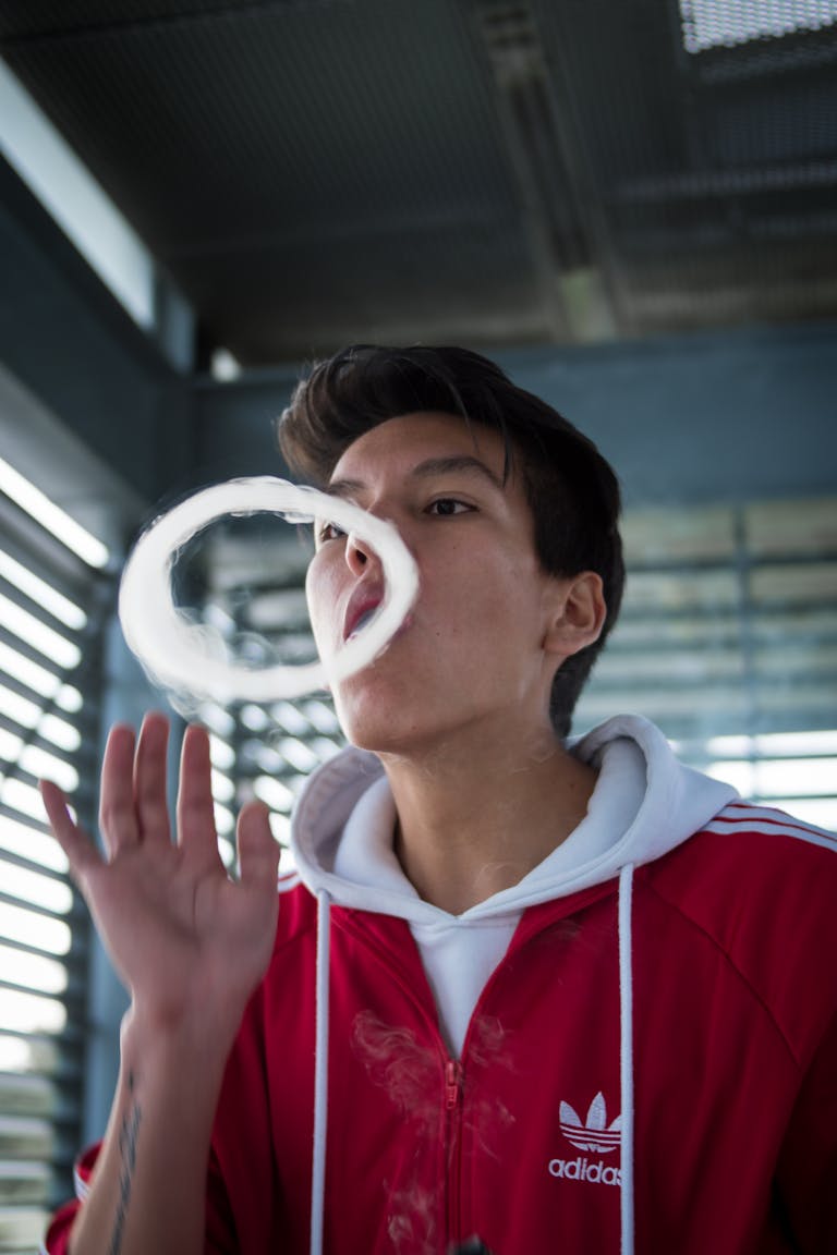 Portrait of a young man blowing vape ring in an urban indoor setting.