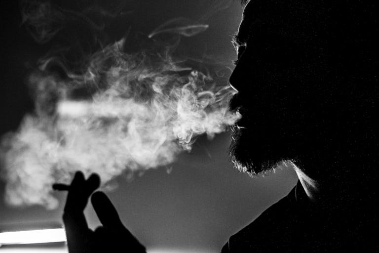 Dramatic black and white photo of a man's silhouette exhaling smoke, creating an atmospheric effect.