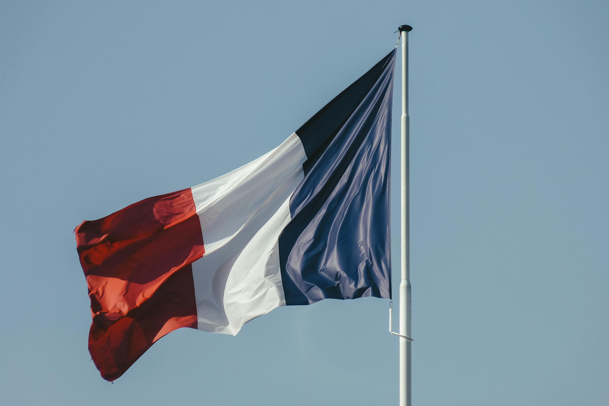 The French national flag waving against a bright blue sky, symbolizing liberty and national pride.